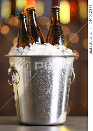 Beer in metal bucket with ice on table against blurred lights Beer in metal bucket with ice on table against blurred lights 140912881