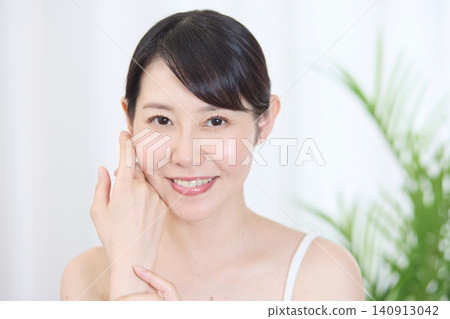 A smiling woman checks the condition of her skin by touching her cheek with her finger. A smiling woman checks the condition of her skin by touching her cheek with her finger. 140913042