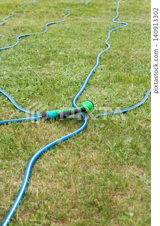 Garden hose and spray nozzle on green lawn with long hose extending into the distance Garden hose and spray nozzle on green lawn with long hose extending into the distance 140913302
