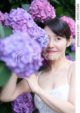 A woman surrounded by hydrangeas, displaying a serene expression. 140913586
