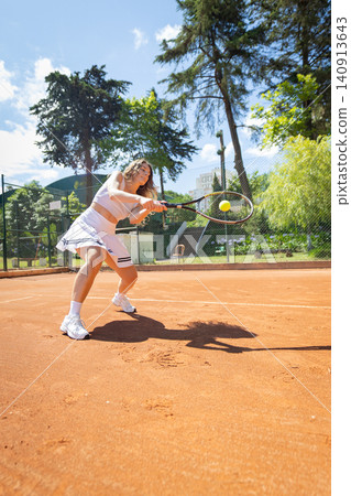 Tennis player hits a ball on a clay court in bright sunlight during a practice session Tennis player hits a ball on a clay court in bright sunlight during a practice session 140913643