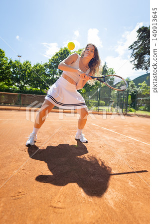 Woman plays tennis on a clay court during the day with a yellow ball in clear sky Woman plays tennis on a clay court during the day with a yellow ball in clear sky 140913645