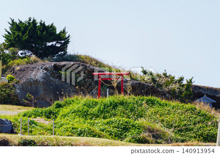 A small red torii gate stands atop a small hill. A small red torii gate stands atop a small hill. 140913954