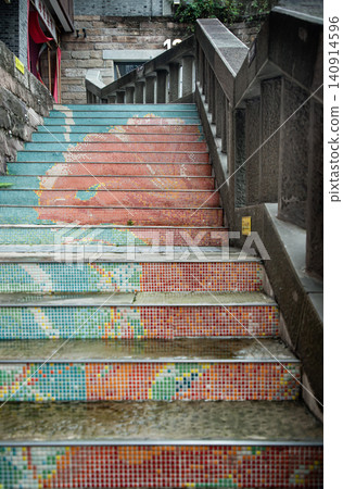 an outdoor stone staircase features vibrant, colorful mosaic tiled risers leading upward alongside a stone banister in an urban or historic setting. an outdoor stone staircase features vibrant, colorful mosaic tiled risers leading upward alongside a stone banister in an urban or historic setting. 140914596