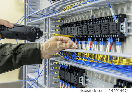 一名電工正在給許多黑色繼電器端子接線;控制面板上有成排的黃色和藍色電纜。 一名電工正在給許多黑色繼電器端子接線;控制面板上有成排的黃色和藍色電纜。 140914674