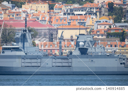 Naval ship docked near city buildings in sunny weather with clear skies during midday in a coastal area Naval ship docked near city buildings in sunny weather with clear skies during midday in a coastal area 140914885