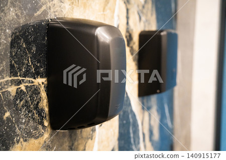 Black wall mounted soap dispenser in a modern commercial restroom with marble wall finish. Hygiene equipment and touch free sanitation for office and public facilities Black wall mounted soap dispenser in a modern commercial restroom with marble wall finish. Hygiene equipment and touch free sanitation for office and public facilities 140915177