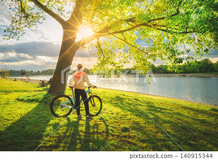 Woman riding a mountain bike near lake at sunset in summer Woman riding a mountain bike near lake at sunset in summer 140915344