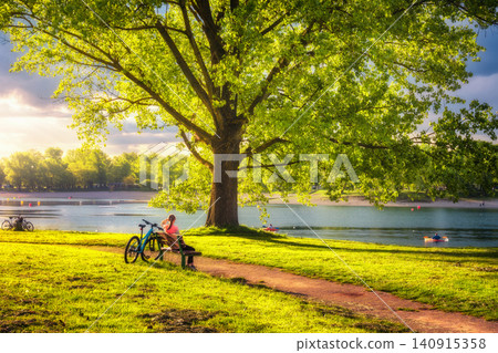 Woman sitting on bench and mountain bike, green trees Woman sitting on bench and mountain bike, green trees 140915358