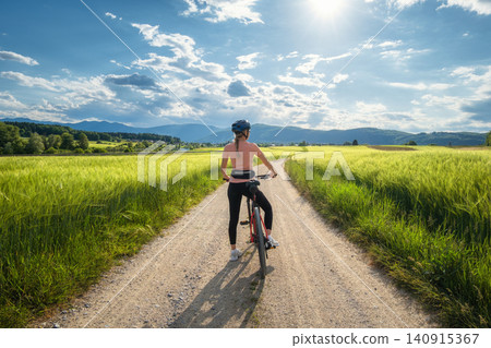 Woman riding mountain bike on dirt road and green wheat fields Woman riding mountain bike on dirt road and green wheat fields 140915367