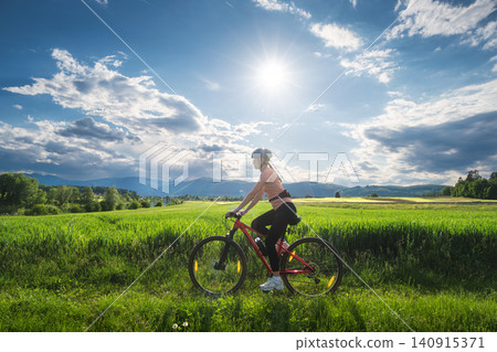Female cyclist riding mountain bike through vibrant green meadow Female cyclist riding mountain bike through vibrant green meadow 140915371