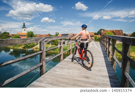 Female cyclist with mountain bike standing on old wooden bridge Female cyclist with mountain bike standing on old wooden bridge 140915374