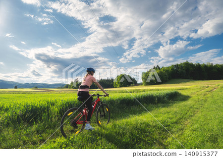 Female cyclist riding mountain bike on path through green fields Female cyclist riding mountain bike on path through green fields 140915377