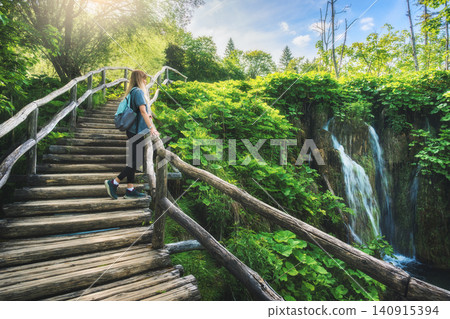 Young woman with backpack with backpack standing on wooden stairs Young woman with backpack with backpack standing on wooden stairs 140915394