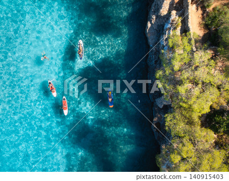 Aerial drone view of colorful kayaks, rocky coastline, blue sea Aerial drone view of colorful kayaks, rocky coastline, blue sea 140915403