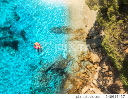 Aerial view of woman on pink swim ring in blue sea, sandy beach Aerial view of woman on pink swim ring in blue sea, sandy beach 140915437