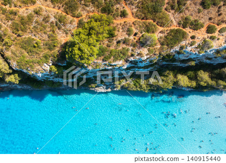 Aerial drone view of turquoise sea, swimmers, rocky coastline Aerial drone view of turquoise sea, swimmers, rocky coastline 140915440