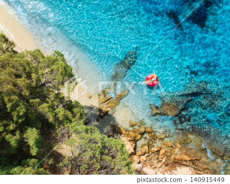Aerial view of woman on pink swim ring in blue sea, sandy beach Aerial view of woman on pink swim ring in blue sea, sandy beach 140915449