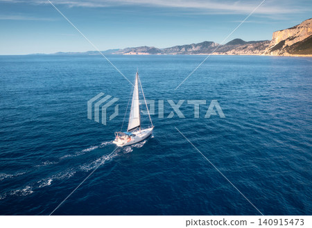 Aerial view of floating sailboat and rocky sea coast at sunny day Aerial view of floating sailboat and rocky sea coast at sunny day 140915473