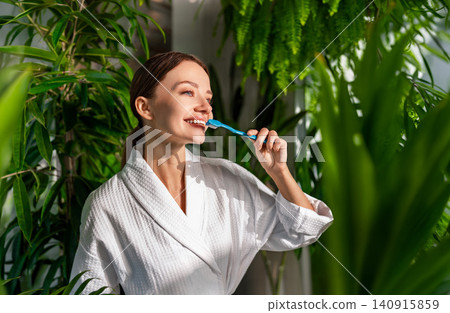Happy young Caucasian woman brushing teeth in a bright bathroom filled with green houseplants Happy young Caucasian woman brushing teeth in a bright bathroom filled with green houseplants 140915859