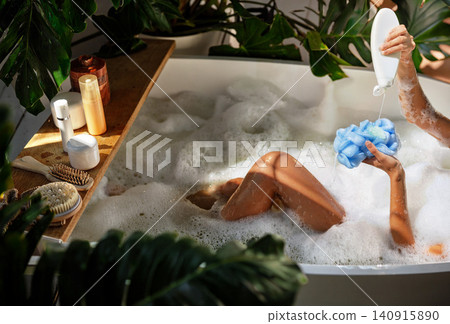 Caucasian young woman pouring body wash on sponge in bubble bath at home bathroom Caucasian young woman pouring body wash on sponge in bubble bath at home bathroom 140915890
