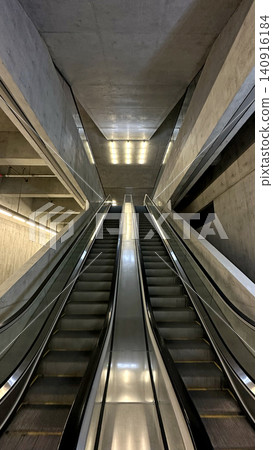 Modern escalators ascend between raw concrete walls in a minimalist architectural space Modern escalators ascend between raw concrete walls in a minimalist architectural space 140916184