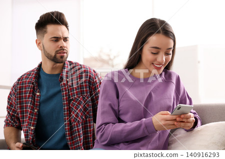 Distrustful young man peering into girlfriend's smartphone at home 140916293