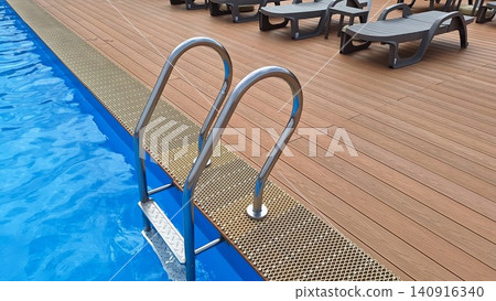 Elegant Swimming Pool Area Featuring Modern Ladders and Stylish Loungers on a Warm Day 140916340