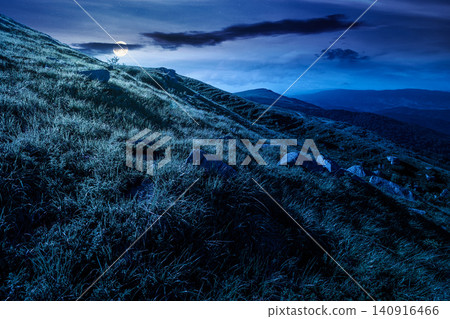mountain landscape with grass and rock on a slope at night. mysterious view in to the distant valley of carpathian mountains. full moon over mountainous fantasy scenery of ukraine in summer mountain landscape with grass and rock on a slope at night. mysterious view in to the distant valley of carpathian mountains. full moon over mountainous fantasy scenery of ukraine in summer 140916466