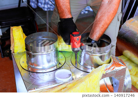 HVAC worker is assembling duct metal parts using screwdriver wearing gloves. HVAC worker is assembling duct metal parts using screwdriver wearing gloves. 140917246