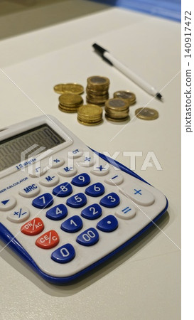 Calculator, Coins, and Pen on a White Desk Calculator, Coins, and Pen on a White Desk 140917472