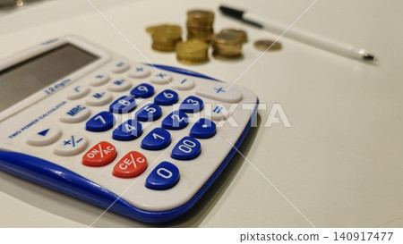 Calculator and Coins on a White Surface Calculator and Coins on a White Surface 140917477