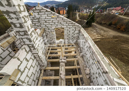 Interior of future cottage, energy saving walls of large white hollow foam insulation blocks and temporary wooden scaffolding frame. Construction, masonry, modern technology concept. Interior of future cottage, energy saving walls of large white hollow foam insulation blocks and temporary wooden scaffolding frame. Construction, masonry, modern technology concept. 140917520