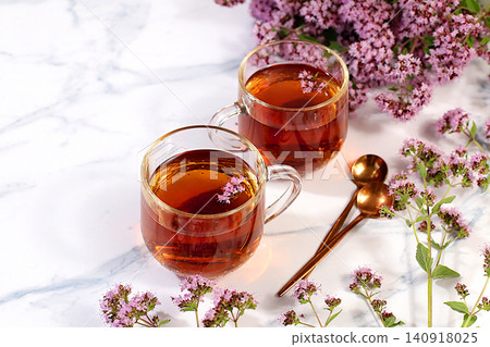 Medicinal herbal tea or Oregano infusion in a glass cup with flowers, alternative traditional medicine concept, estrogen source, menopause remedy, green pharmacy advertisement, Medicinal herbal tea or Oregano infusion in a glass cup with flowers, alternative traditional medicine concept, estrogen source, menopause remedy, green pharmacy advertisement, 140918025