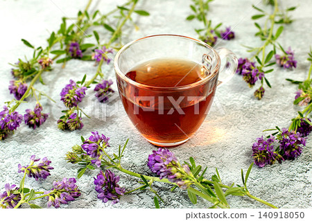 Medicinal herbal tea or Alfalfa infusion in a glass cup with flowers, alternative traditional medicine concept, estrogen source, green pharmacy advertisement, collection of useful herbs Medicinal herbal tea or Alfalfa infusion in a glass cup with flowers, alternative traditional medicine concept, estrogen source, green pharmacy advertisement, collection of useful herbs 140918050