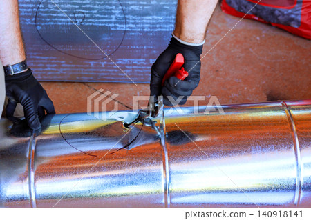 Contractor is using tools to cut metal duct pipe setting during HVAC assembly installation. Contractor is using tools to cut metal duct pipe setting during HVAC assembly installation. 140918141
