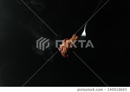 一隻熱氣騰騰的烤雞被叉子叉住,在黑色背景下顯得格外醒目。 一隻熱氣騰騰的烤雞被叉子叉住,在黑色背景下顯得格外醒目。 140918683