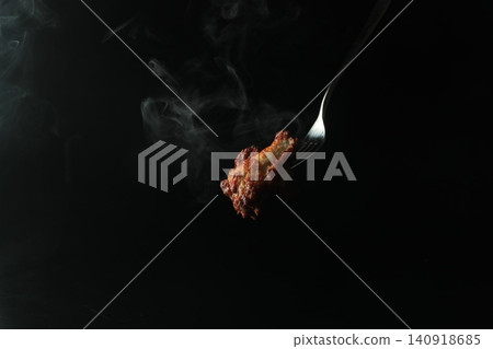 一隻熱氣騰騰的烤雞被叉子叉住,在黑色背景下顯得格外醒目。 一隻熱氣騰騰的烤雞被叉子叉住,在黑色背景下顯得格外醒目。 140918685