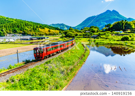 The Limited Express Yufu runs through the early summer countryside with Mount Yufu in the background on the Kyudai Main Line. The Limited Express Yufu runs through the early summer countryside with Mount Yufu in the background on the Kyudai Main Line. 140919156