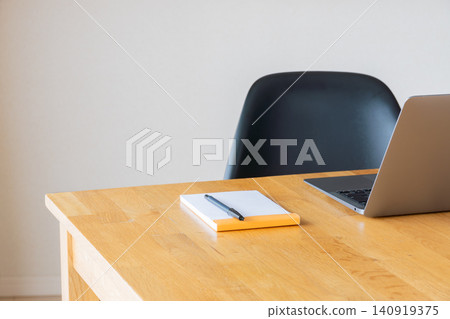 A wooden desk with a laptop and notepad on it, against a white wall. A wooden desk with a laptop and notepad on it, against a white wall. 140919375