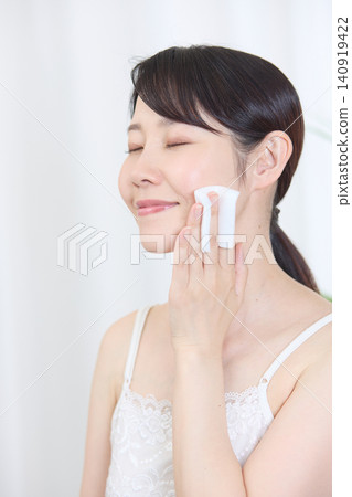 一位面帶微笑的日本女子用棉球擦拭臉頰。 一位面帶微笑的日本女子用棉球擦拭臉頰。 140919422