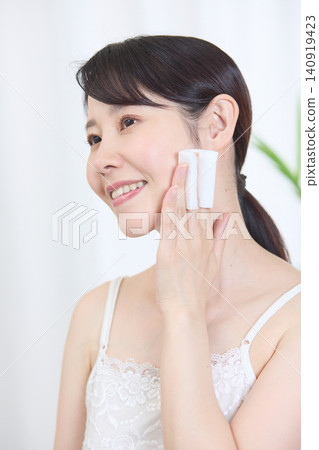 一位面帶微笑的日本女子用棉球擦拭臉頰。 一位面帶微笑的日本女子用棉球擦拭臉頰。 140919423