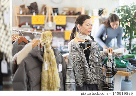 Middle-aged woman choosing winter coat in clothing store Middle-aged woman choosing winter coat in clothing store 140919859