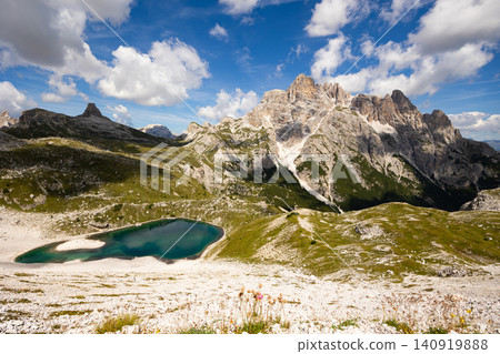 White sandy-rocky slope descends to shore of small lake in Laghi dei piani area with emerald water 140919888