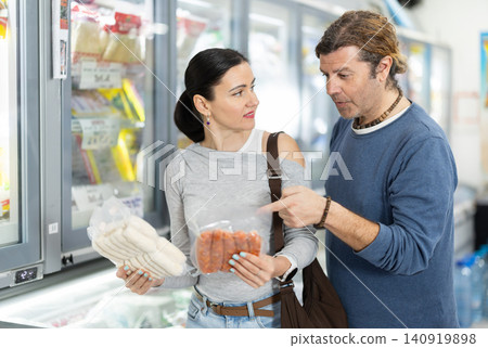 Couple in supermarket choose cooled raw sausages Couple in supermarket choose cooled raw sausages 140919898