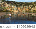 Young boy walks through the shallow lagoon at Iztuzu Beach near Dalyan, Turkey. Peaceful family travel moment surrounded by water, cliffs and protected coastal nature during summer vacation. 140919948