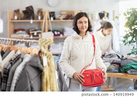 Woman looks at products in store and selects handbag. Woman looks at products in store and selects handbag. 140919949