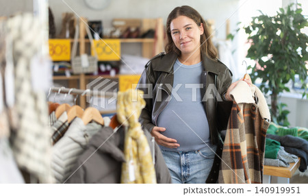 Pregnant woman chooses plaid jacket in clothing store 140919951