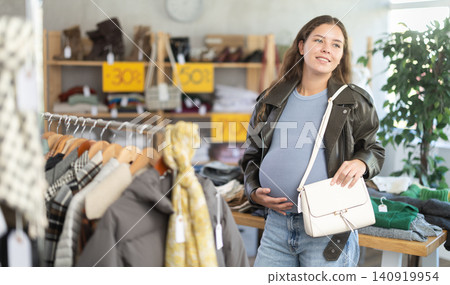 Pregnant woman choosing handbag in clothing store Pregnant woman choosing handbag in clothing store 140919954