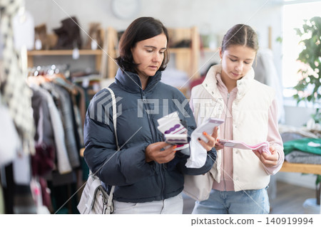 Mother and teen daughter looks at products in store and selects cotton socks. Mother and teen daughter looks at products in store and selects cotton socks. 140919994
